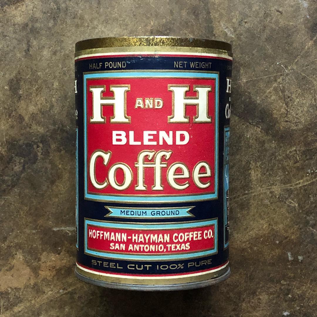 Front-on view of the half-pound tin on a stone surface, showing the full paper label: the "HALF POUND / NET WEIGHT" band along the top, the H AND H BLEND Coffee lockup in red and pale blue, the MEDIUM GROUND banner, the HOFFMANN-HAYMAN COFFEE CO., SAN ANTONIO, TEXAS panel, and the STEEL CUT 100% PURE footer. A second H and H Blend tin is partially visible directly behind.