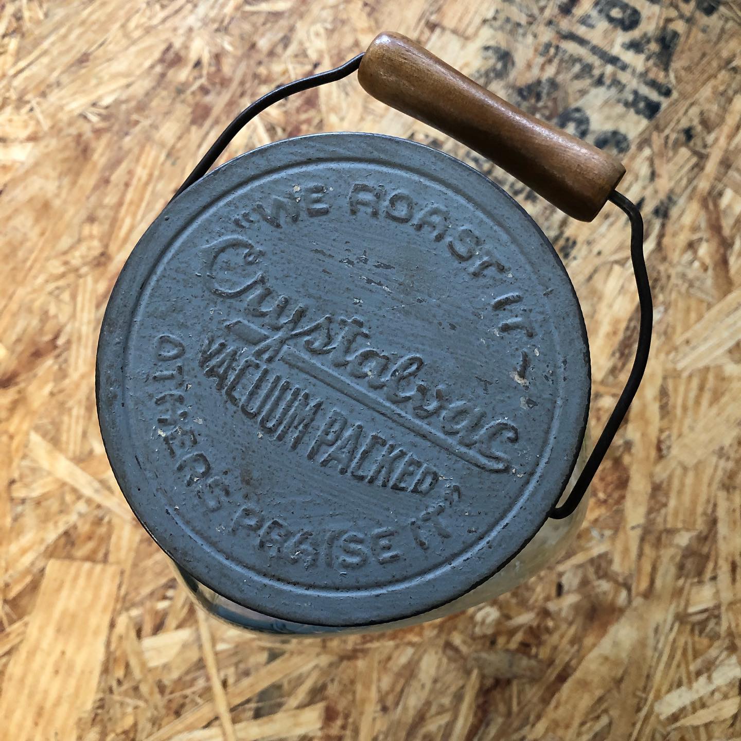 Top-down view of the metal lid: "WE ROAST IT / Crystalvac VACUUM PACKED / OTHERS PRAISE IT" with wire bail and wooden handle