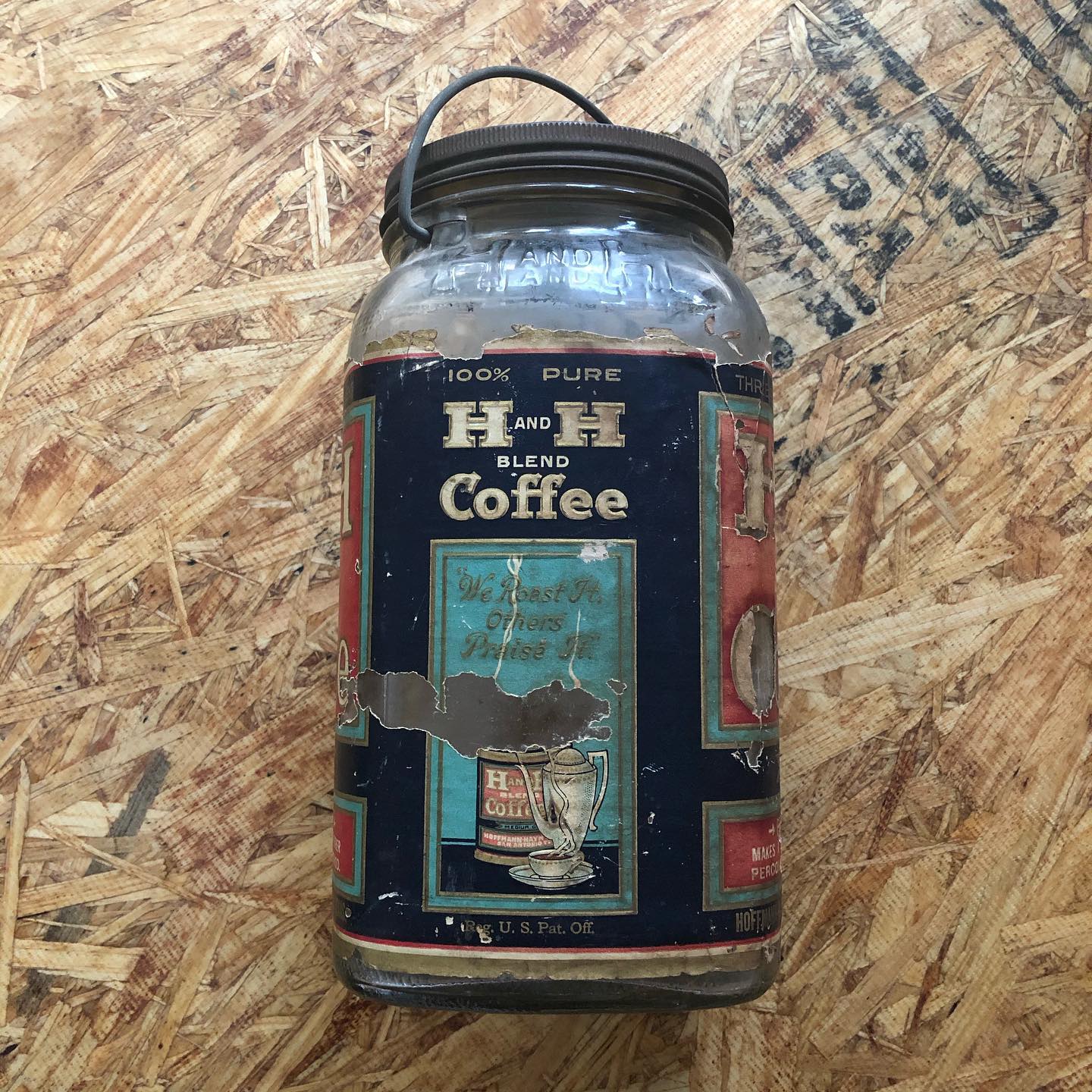 Reverse of the same three-pound Crystalvac jar, showing the "100% PURE / H AND H BLEND Coffee" side of the paper label with a central illustration of an H and H Blend tin beside a steaming coffee pot and cup, the "We Roast It, Others Praise It" banner in script, and "Reg. U.S. Pat. Off." along the base. The edges wrap to the front panel ("THREE POUNDS") on the right. "H AND H" embossing is faintly visible on the bare glass above the label, and the original black metal screw lid with wire bail is still in place.