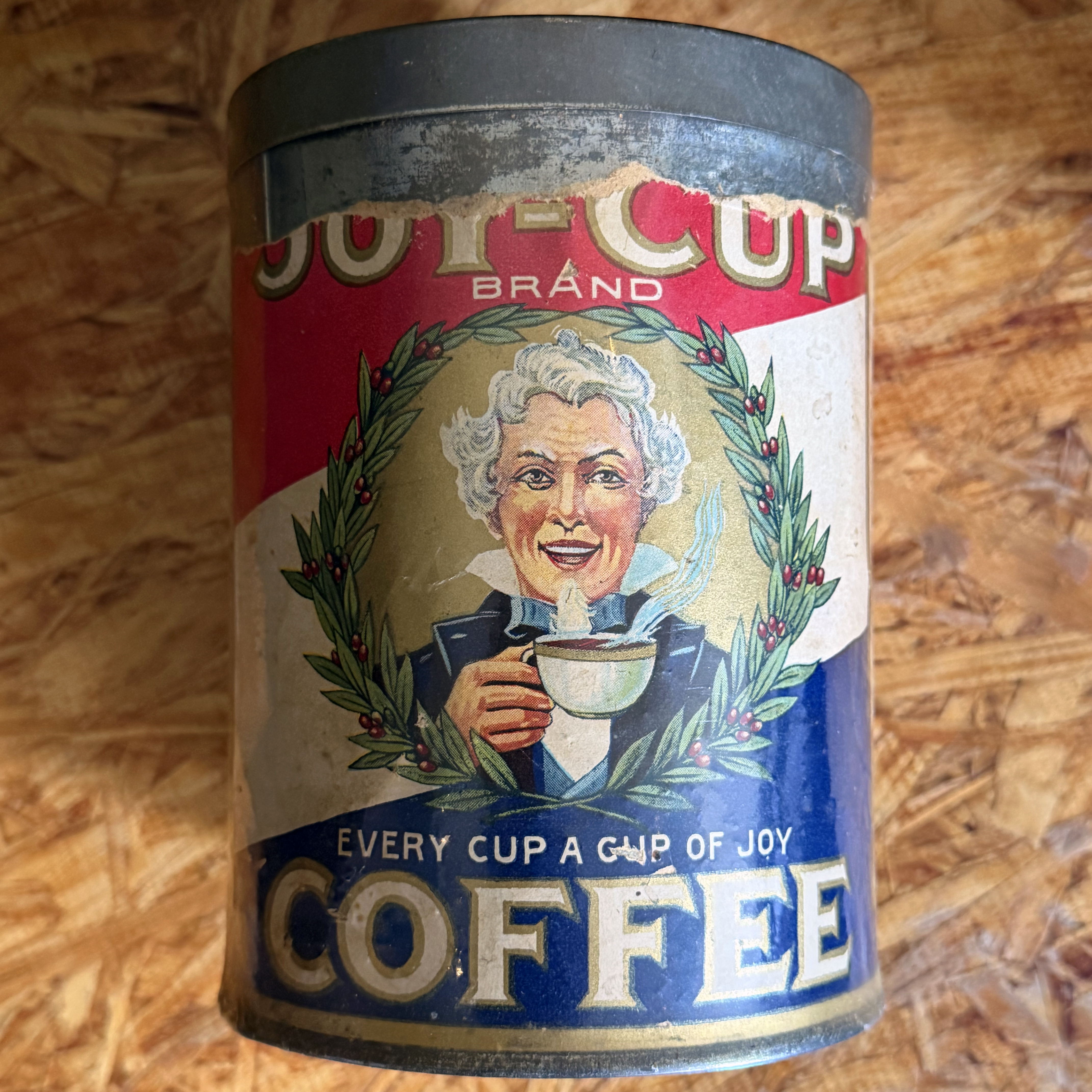 Joy-Cup Brand Coffee tin — in-hand front view on OSB