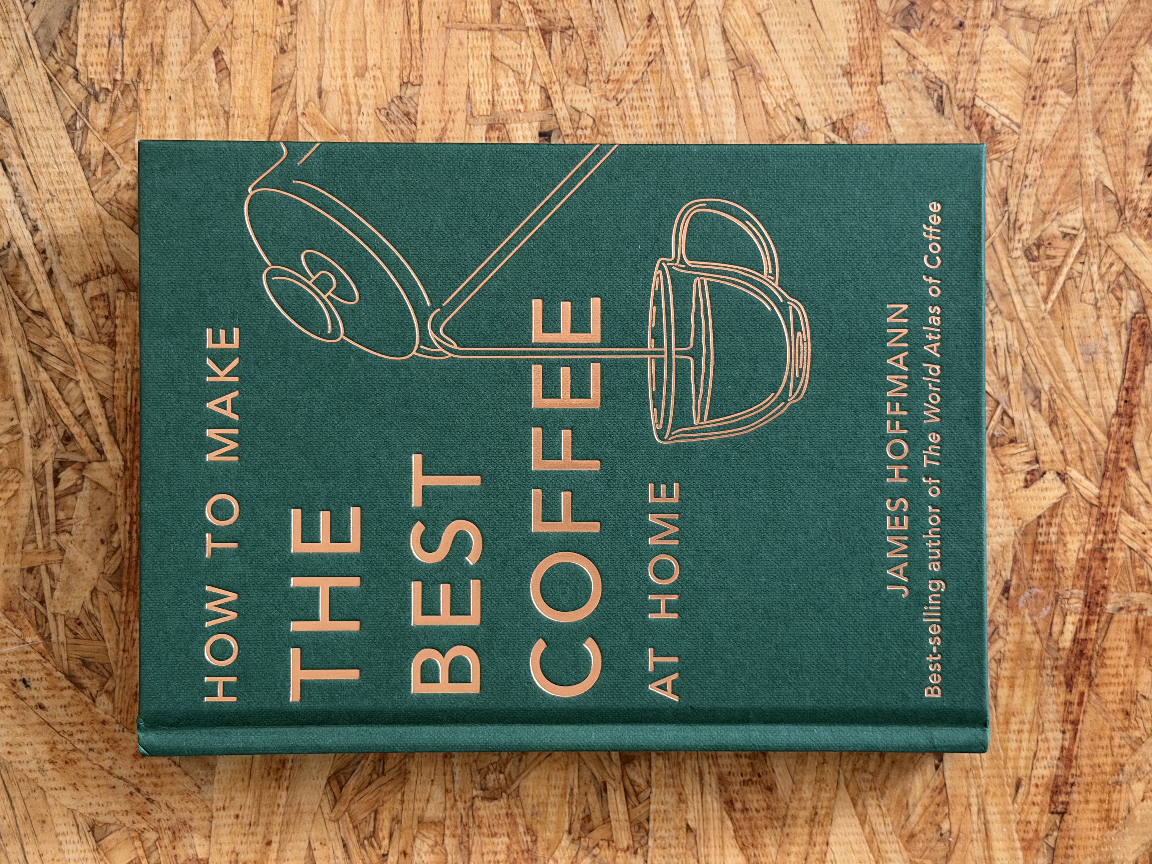 How To Make The Best Coffee At Home by James Hoffmann — forest-green hardcover with copper foil line art of a hand grinder and gooseneck kettle, photographed 2026-06-06