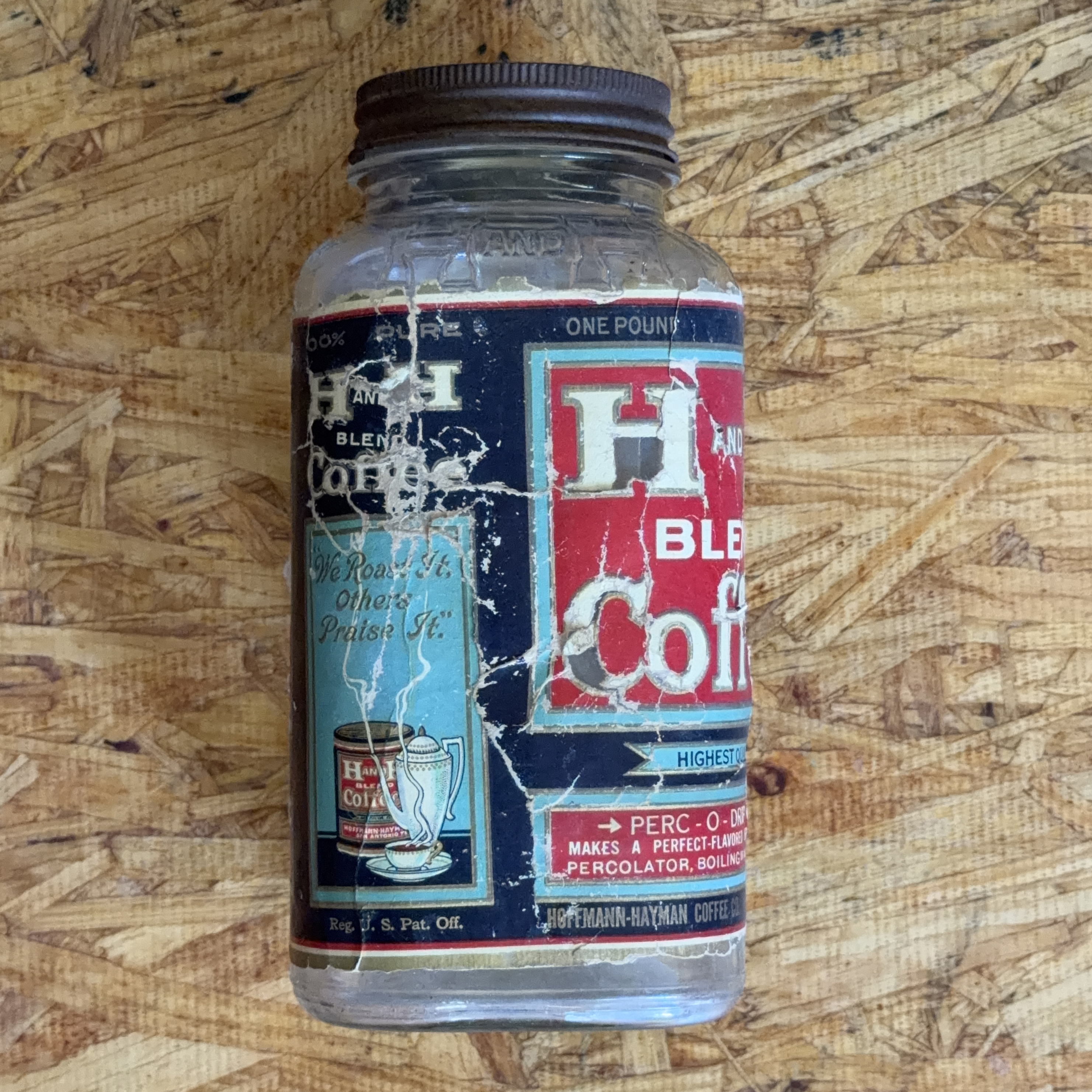 H and H Blend Coffee one-pound Crystalvac jar with a reassembled, heavily crackled paper label showing the We Roast It Others Praise It side panel with coffee pot vignette, photographed 2026-07-21