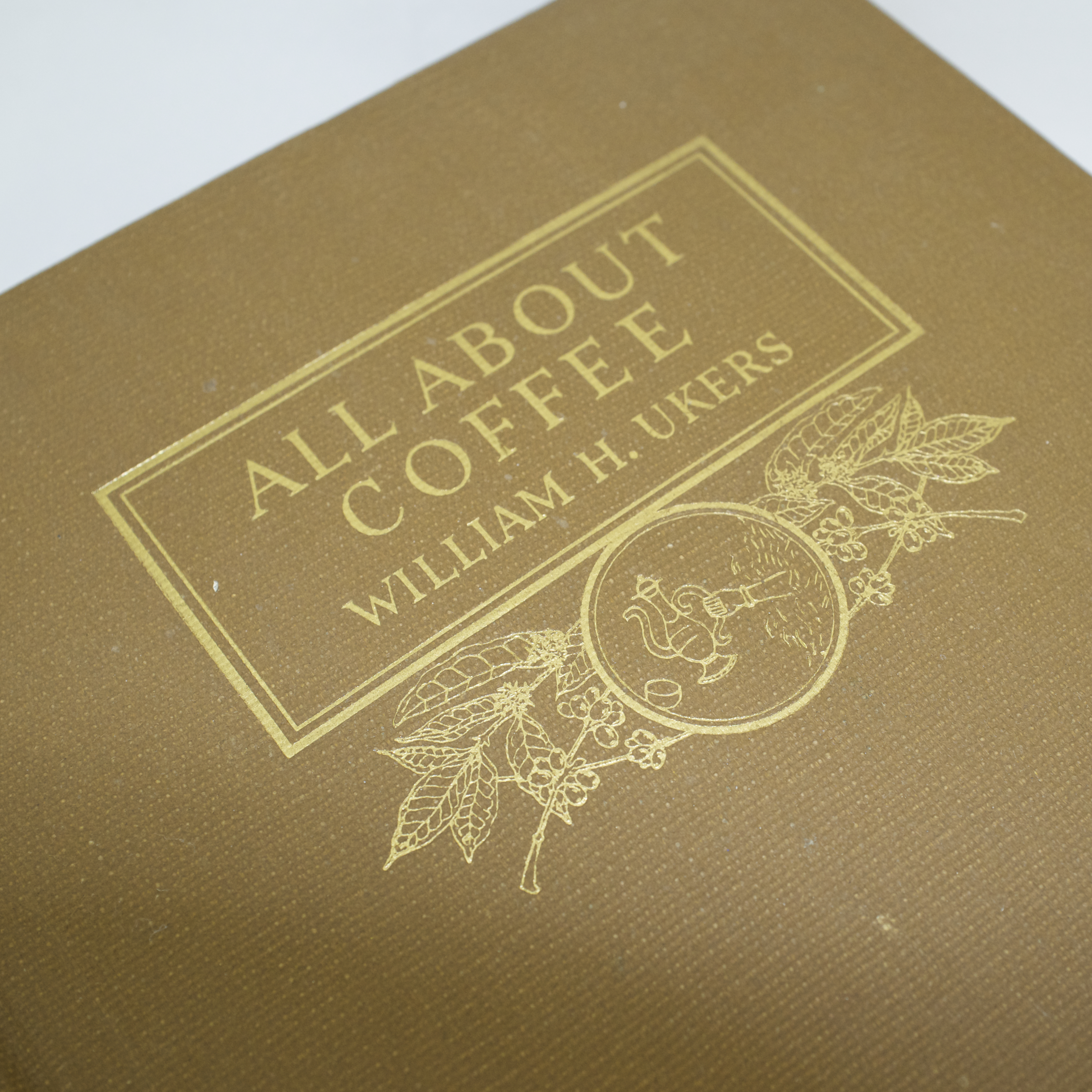 Tan cloth cover of All About Coffee by William H. Ukers, gold title block and botanical coffee illustration
