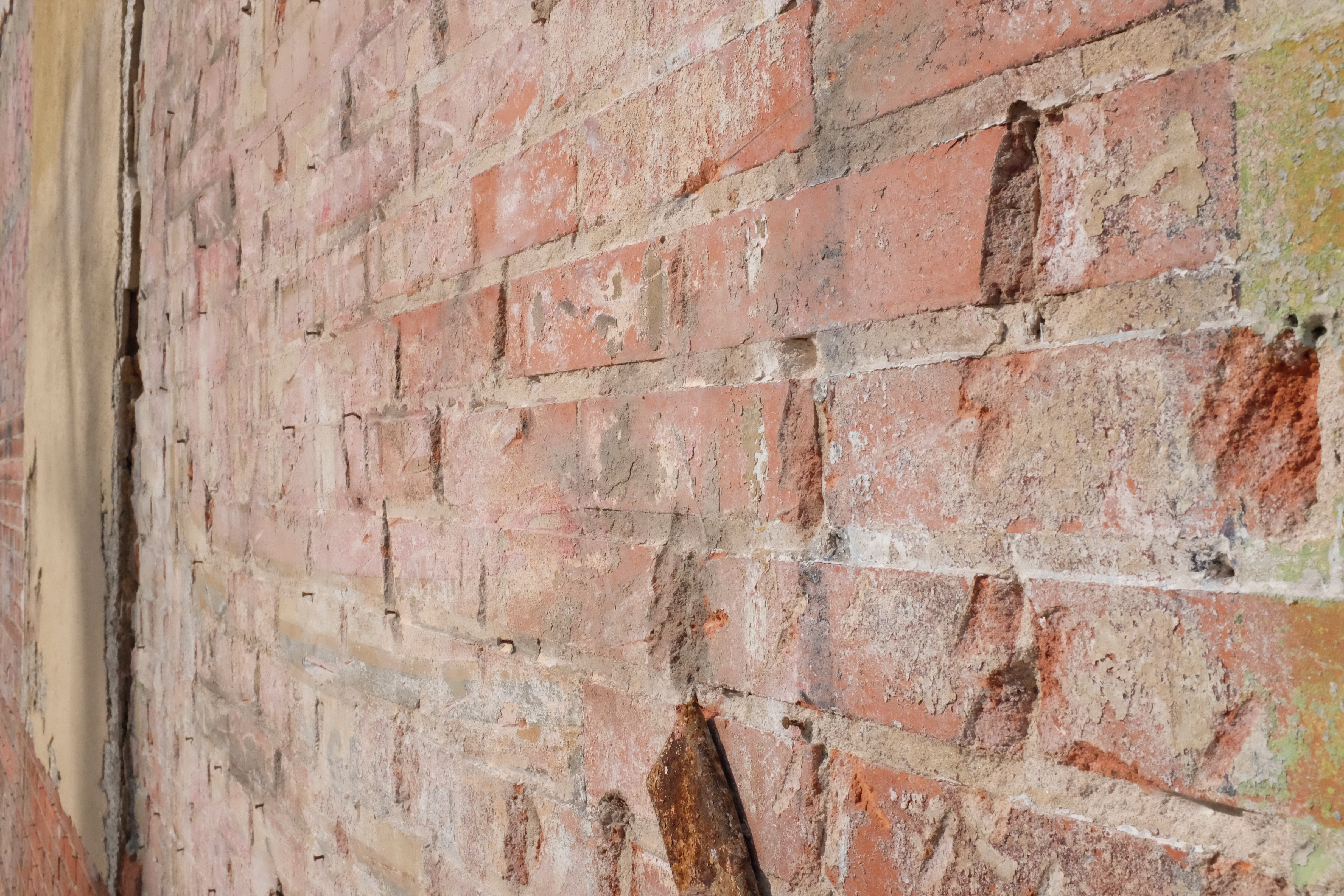 South-face brick — stucco strip at left, nail remnants, faint paint ghosts