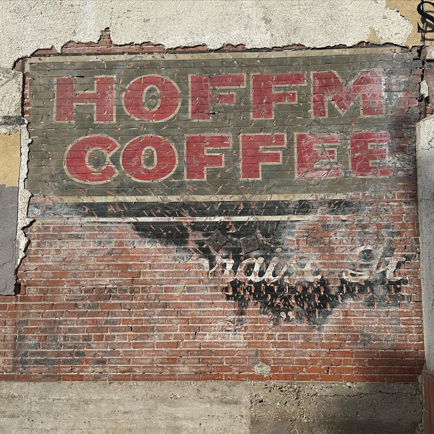 Stucco peeled back on brick to show hand-painted H and H lettering; a period rounded H and H tin with embossed lid sits beside the find for scale.