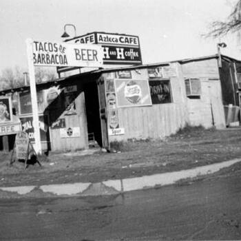 Black-and-white photograph **1949** — **Exterior of Azteca Cafe**, San Antonio, Texas (**General Photograph Collection**, UTSA Digital Collections — collection **p9020coll008**, item **9664**, `digital.utsa.edu`): small street-front cafe with painted signs including **tacos de barbacoa**, **H and H coffee**, and **beer** (per UTSA item metadata); **700×386** institutional JPEG from ContentDM API — **not in the museum collection**