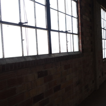 **19 February 2014** (**Sony Cyber-shot DSC-RX100**) — interior along an **exposed brick** wall of the Hoffmann-Hayman plant: two tall **steel-sash** window banks with **chain-and-lever** vent operators, strong backlight through wire or textured glass, board-formed concrete sill.