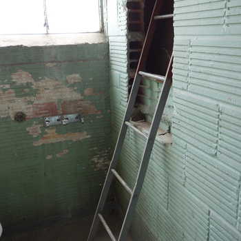 **2 May 2014** (**Sony DSC-RX100**) — companion view: grey **metal ladder** rising into a **rectangular opening** in **ribbed / fluted green** glazed or structural tile, adjoining wall with **peeled paint** exposing red brick; concrete slab floor — Hoffmann-Hayman interior exploration.