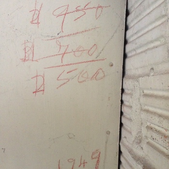 **8 June 2014** (**Apple iPhone 5**) — flat panel beside **scored** wall at the Hoffmann-Hayman factory: **red grease-pencil** tally marks **# 950**, **# 700** (struck through), **# 500**, and the year **1949**; two fasteners through the board — informal stock or pricing note on the fabric.