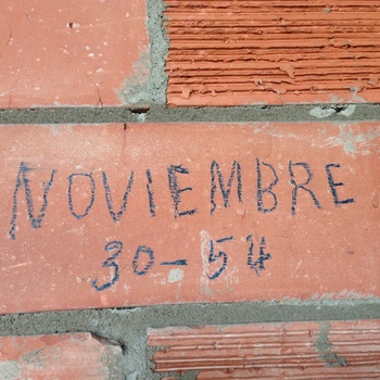 **29 August 2014** (**Apple iPhone 5**) — close-up on **interior brick** at Hoffmann-Hayman: ink or ballpoint **NOVIEMBRE** and **30–54** on a stretcher beside **ridged** neighbor units — read here as **30 November 1954** trades documentation or graffito in the expansion chronology corpus.
