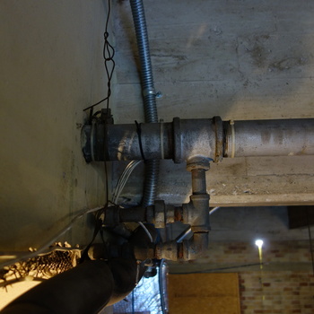 **5 October 2014** (**Sony DSC-RX100**) — **galvanized steel** pipe run with **tee** and drops, **flexible metal conduit (BX)**, and loose white conductors against **board-grained concrete** vault-zone soffit at Hoffmann-Hayman — **mechanical companion** to other **same-date vault** documentation in this gallery.