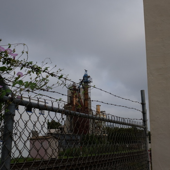 **8 September 2016** (**Fujifilm X100T**) — **chain-link** with **barbed wire** and morning-glory vine; **rusted vertical process tower** with **blue** headworks, **rails** in middle ground, cream Hoffmann-Hayman mass at frame edge — **perimeter** context under **overcast**.