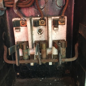 **17 November 2016** (**Apple iPhone 6s**) — obsolete **three-pole knife switch** or **fusible disconnect** with **white ceramic insulators**, **fabric-rubber** phase leads, heavy **rust** and dust in a dark hinged enclosure — **pre-breaker** plant distribution at Hoffmann-Hayman.