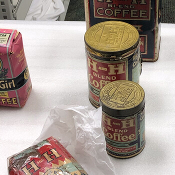 Color photograph **15 October 2019** — grouped **H and H Blend** packaging on white foam: **three-pound** rectangular tin with top closure and accession string, a **cylindrical** tin with **embossed gold lid** reading **'AN H AND H PRODUCT'** and **'We Roast It Others Praise It'**, a smaller **cylindrical** tin with **'H AND H BLEND COFFEE'**, **'VACUUM PACKED'**, **'STEEL CUT 100% PURE'**, and roaster mark for **Hoffmann-Hayman Coffee Co. San Antonio, Texas**; a **brick** of coffee in **sealed clear archival wrap** on tissue; a **Texas Girl** pack edge at left — Witte **institutional** staging, **not in the project’s museum collection**