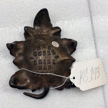 Color photograph **15 October 2019** — **bottom** of a **cast leaf-form ashtray** issued as a **premium** for **H and H coupon** redemptions (customers mailed in coupons to receive the piece): stacked embossed capitals on the **base** read **'EAT'** / **'SMOKE'** / **'DRINK'** / **'H & H'** / **'COFFEE'**; **Witte** accession **'KS 193'** on oval sticker and large rectangular string tag; white foam — same **coupon premium** type as other packaged-goods loyalty offers of the period; **not in the project’s museum collection**