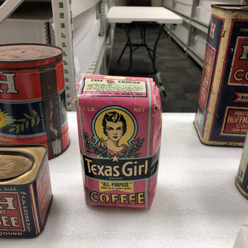 Color photograph **15 October 2019** — **Texas Girl** 1 lb bag (same graphic system as the single-bag frame) as the **center** of a wider foam staging: **H and H Blend** half-pound **'LIGHT HOUSEKEEPERS SIZE'** square tin, large **'VACUUM PACKED'** / **'QUALITY'** cylindrical, tall rectangular **'ROASTED' … Hoffmann'** tin at right — contextual **group** shot from the same **Witte** presentation; **not in the project’s museum collection**