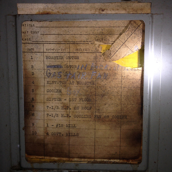 Inside-of-door circuit directory of the older **Trumbull Electric Mfg. Co.** breaker panel at the Hoffmann-Hayman factory (Plainville, Conn., USA — pre-1950 vintage, with a yellow Underwriters Laboratories 'INSPECTED ELECTRIC CABINET FRONT' approval label visible at the upper right) — a typed/printed paper directory taped inside the panel door listing the **primary process-equipment circuits** in numbered order, with a mix of pre-printed typewriter labels and later pen/marker corrections: '1 ROASTER MOTOR', '2 [ ] MOTOR / IN [BACK?]', '3 GAS-AIR FAN', '4 ELEVATOR-AT ROASTER', '5 COOLER / Box', '6 SIFTER - 1ST FLOOR', '7 7-1/2 H.P. ON ROOF', '8 7-1/2 H.P. COOLING FAN ON COOLER', '9 1 - #12 MILL', '10 4 GOVT. MILLS' — the panel covering the building's main coffee-process line on the first floor (roaster, cooler, sifter, mills, elevator at the roaster) and rooftop HVAC, distinct from the later second-floor Federal Pacific panel that covers the Tea Machine, air conditioning, and a separate second-floor sifter circuit