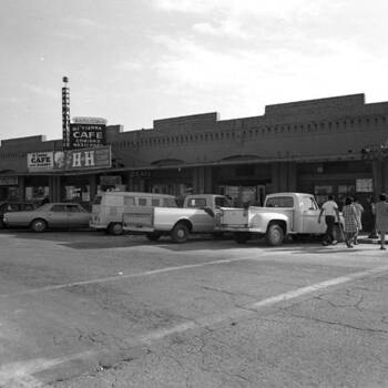 Black-and-white photograph — **Mi Tierra Cafe and Bakery**, **218 Produce Row**, San Antonio, Texas (**Ray Howell Photograph Collection**, UTSA Digital Collections — collection **p9020coll4**, item **412**): street view with **vehicles** parked at the cafe; **Master Chef Coffee** (H and H hotel-and-restaurant trade brand) **signage** on the Mi Tierra building; at right, corner of **Produce Row** and **S. San Saba Street**, the former entrance to **Tony's Wholesale Grocery and Produce Company** (per UTSA item description; finding aid text quotes the sign as 'Master **Chief**' Coffee — treat as the **Master Chef** line); **700×563** institutional JPEG from ContentDM API — **not in the museum collection**